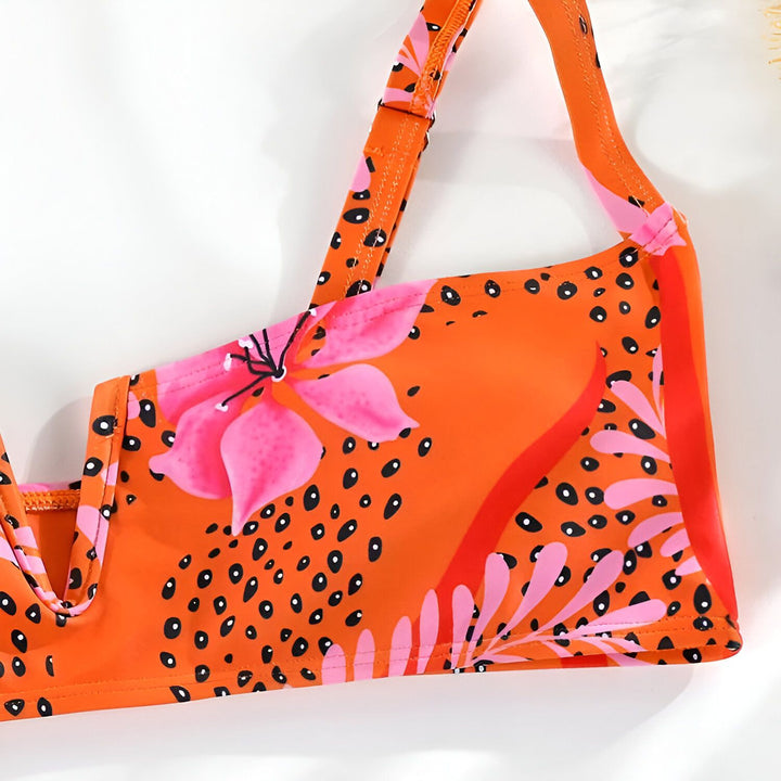 Femme portant un bikini à motifs floraux orange et rose. Haut de bikini avec décolleté en V et bretelles. Bas de bikini taille haute.