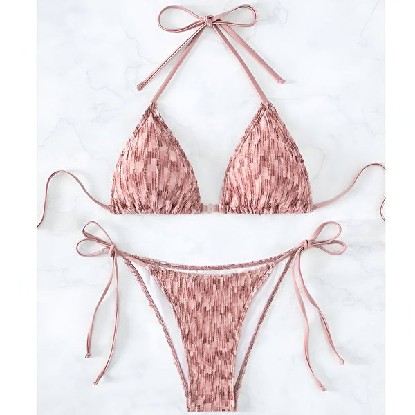 Image d'un bikini deux-pièces rose clair sur fond blanc marbré. Le haut est un triangle avec des liens fins, et le bas est assorti avec des liens sur les côtés. Idéal pour la plage ou la piscine.