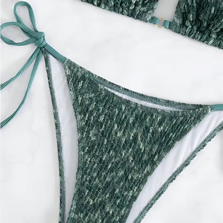 Vue rapprochée d'un haut de bikini texturé vert et blanc, avec des bretelles fines. Le tissu a un motif froissé unique et une fermeture en anneau doré. Idéal pour la plage ou la piscine.