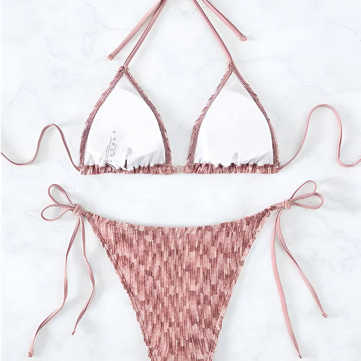 Maillot de bain deux pièces rose avec un motif texturé. Haut triangle à nouer et bas de bikini avec cordons latéraux. Mode estivale et plage.