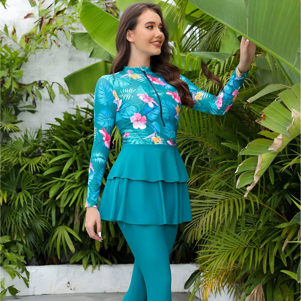 Femme vue de dos portant un maillot de bain bleu-vert à manches longues avec un motif floral, jupe assortie. Arrière-plan de verdure luxuriante. Mode bain, vêtements de plage, style estival.