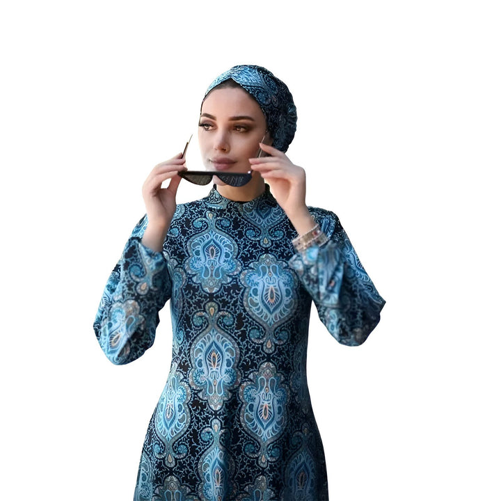Femme portant une robe à motifs bleus et un hijab assorti, tenant des lunettes de soleil. Mode islamique élégante.