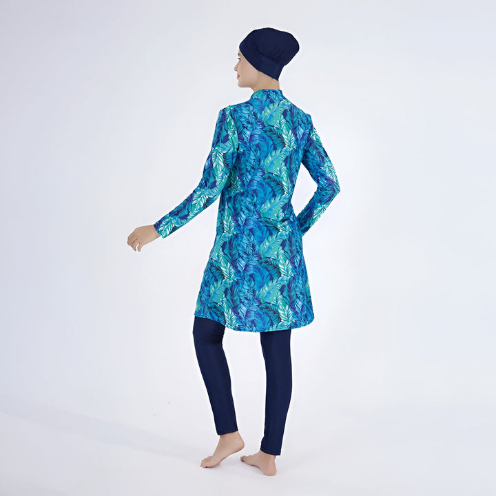 Femme souriante portant un burkini bleu à motifs de feuilles avec hijab et leggings assortis, vêtement de bain modeste pour femmes musulmanes.
