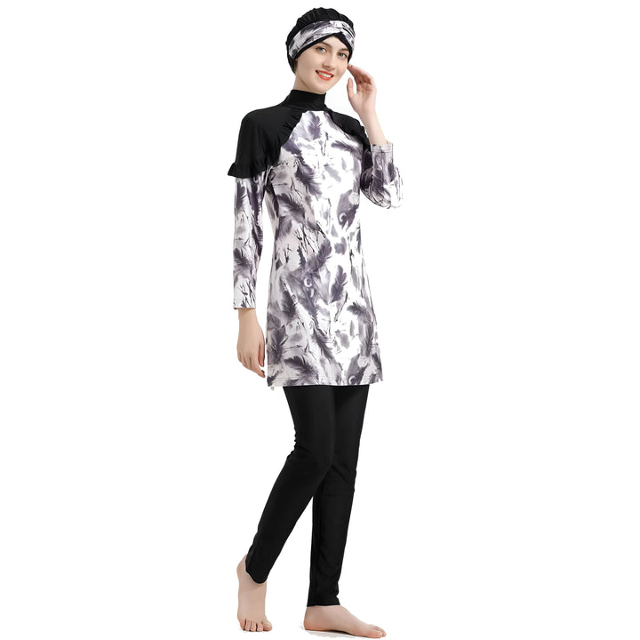 Femme souriante portant un burkini imprimé plumes noir et blanc avec bonnet assorti et legging noir. Vêtement de bain islamique à manches longues.