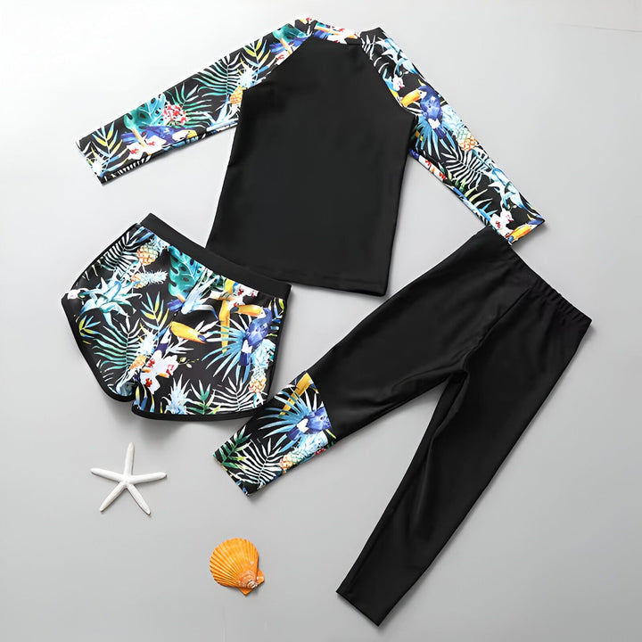 Ensemble de bain femme avec motifs tropicaux : haut manches longues noir, short et legging. Une étoile de mer et un coquillage orange décorent la scène.