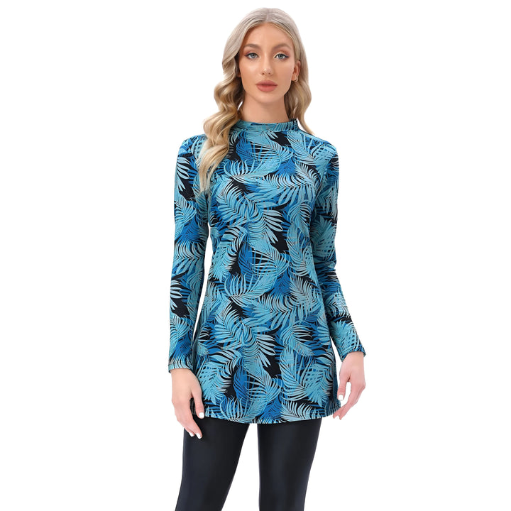 Femme blonde portant un maillot de bain burkini bleu à motifs tropicaux et un bonnet de bain noir. Elle pose avec une main sur la hanche sur un fond blanc.