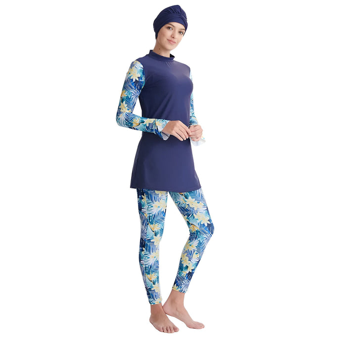 Femme portant un burkini bleu marine avec imprimé floral tropical, vue de dos. Maillot de bain couvrant avec bonnet de bain assorti. Mode plage modeste pour femmes.