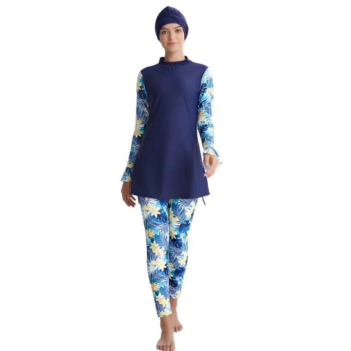 Femme souriante portant un burkini bleu marine avec des motifs floraux bleus et jaunes, manches longues et pantalon assorti. Vêtement de bain modeste et élégant.
