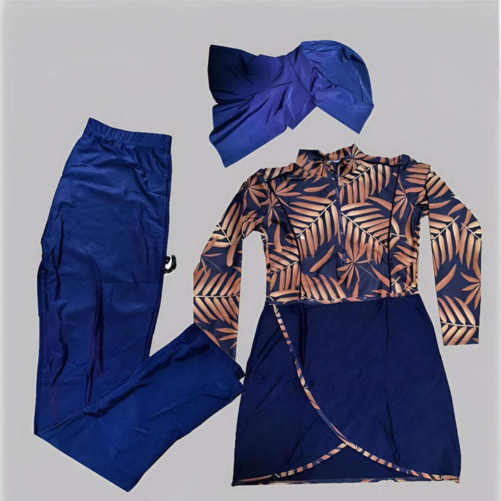 Femme portant un maillot de bain modeste à motifs dorés et noirs avec un turban noir. Le maillot comprend un haut à manches longues, un legging et une jupe portefeuille courte noire. Elle pose devant un fond blanc.