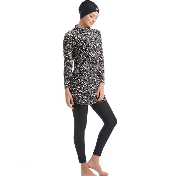 Femme portant un maillot de bain intégral noir et blanc à motifs floraux avec un legging noir, style modeste, manches longues.