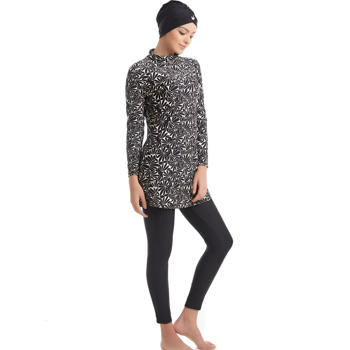 Femme portant un maillot de bain intégral noir et blanc à motifs floraux avec un legging noir, style modeste, manches longues.