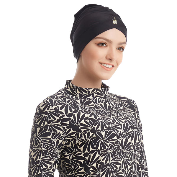 Une femme porte un burkini noir et blanc à motifs floraux avec un bonnet de bain assorti et un legging noir. Vêtements de bain islamiques, mode modeste.