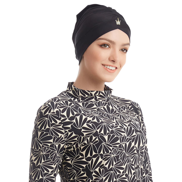 Une femme porte un burkini noir et blanc à motifs floraux avec un bonnet de bain assorti et un legging noir. Vêtements de bain islamiques, mode modeste.