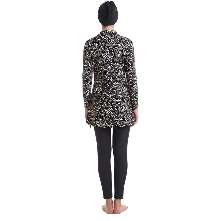 Femme portant un maillot de bain burkini à motifs floraux noirs et blancs avec un bonnet de bain noir. Vêtement de bain modeste à manches longues et pantalon de bain noir.