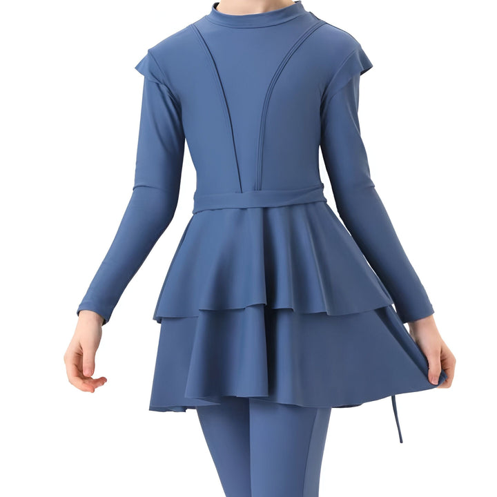 Jeune fille souriante en maillot de bain burkini bleu avec un bonnet assorti, posant avec une planche de bodyboard jaune.