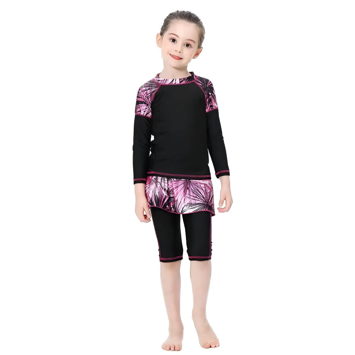 Une fillette souriante porte un maillot de bain intégral noir et rose avec un bonnet de bain assorti. Vêtement de bain couvrant pour enfant.