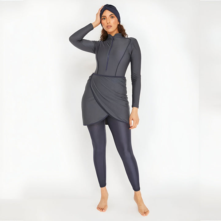 Femme portant un burkini gris foncé avec un turban. Vêtement de bain couvrant avec manches longues et jupe portefeuille intégrée. Mode pudique pour la plage.