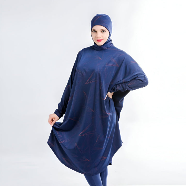 Femme portant un burkini bleu marine à motifs, avec hijab assorti, posant devant un fond blanc. Vêtement de bain islamique.