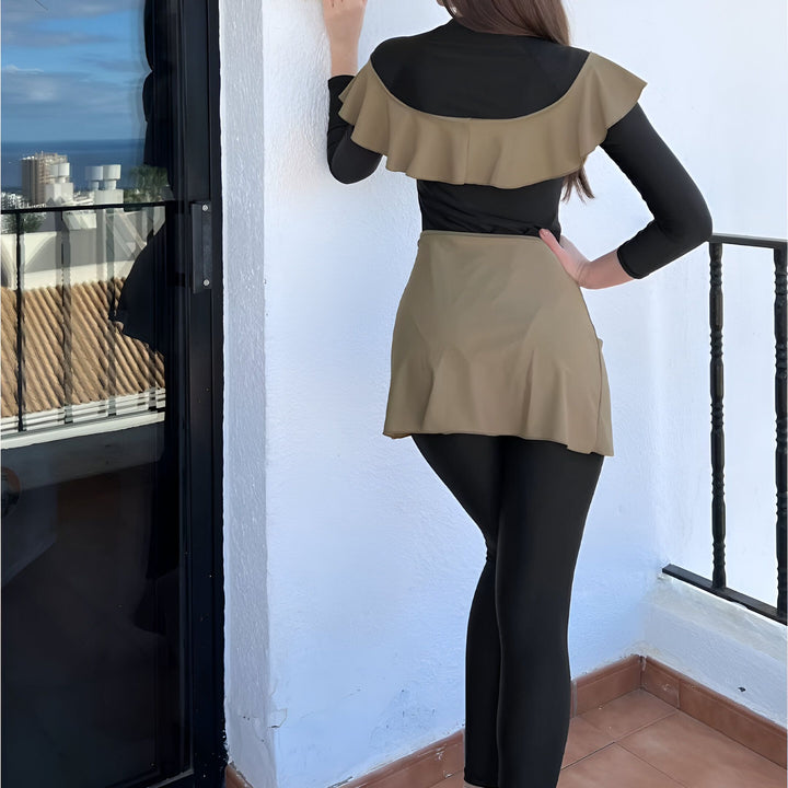 Femme portant un maillot de bain modeste noir et beige avec des volants et une jupe, posant sur un balcon avec vue sur l'océan. Mode islamique, vêtements de plage pudiques, burkini.