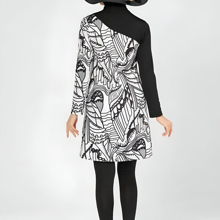 Femme portant un maillot de bain intégral noir et blanc avec motif, un chapeau noir à large bord, sur fond blanc.