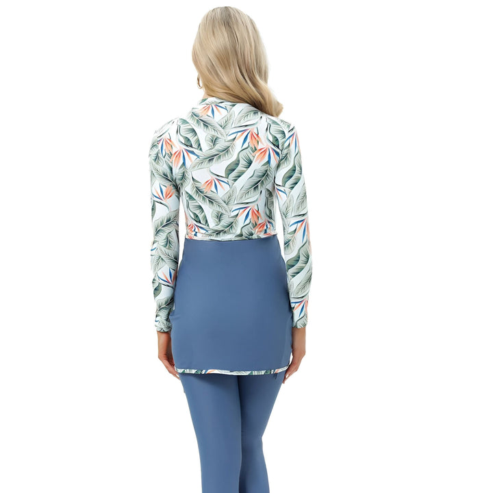 Vue arrière d'une femme blonde portant un maillot de bain de style burkini bleu et blanc à motifs de feuilles et de fleurs tropicales oranges.