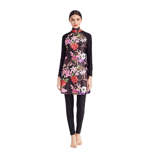 Femme souriante en burkini floral noir, rose et rouge avec un hijab assorti, bras croisés, sur fond blanc. Vêtement de bain modeste, mode islamique, protection solaire.