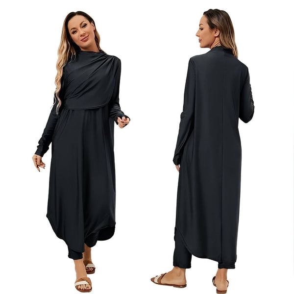 Femme blonde portant une robe de bain noire couvrante, manches longues, devant un mur de pierres blanches avec des cactus. Mode pudique, maillot de bain intégral.