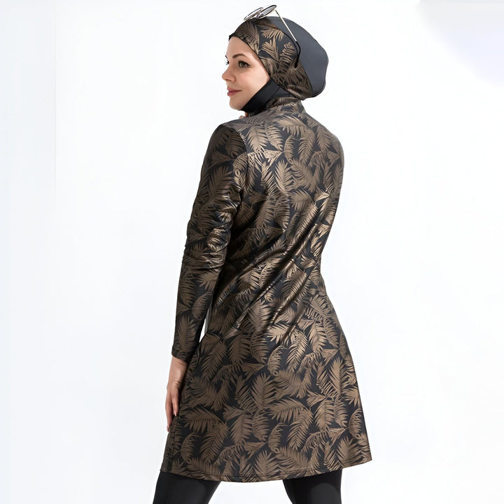 Une femme vue de dos portant un maillot de bain intégral, hijab et lunettes de soleil sur la tête, avec un motif de feuilles de palmier marron et noir sur un fond blanc.