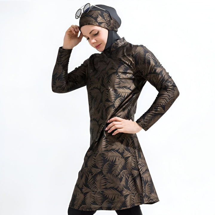 Femme portant un burkini doré à motifs de feuilles, tenant des lunettes. Mode de bain pudique.