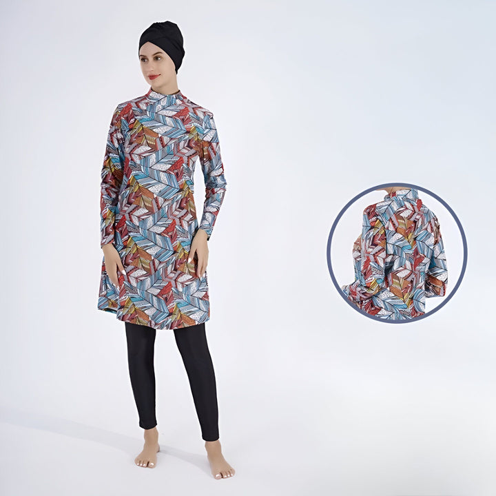 Femme portant un burkini imprimé à manches longues et un hijab noir, posant devant un fond blanc. Vêtement de bain modeste pour femmes musulmanes.