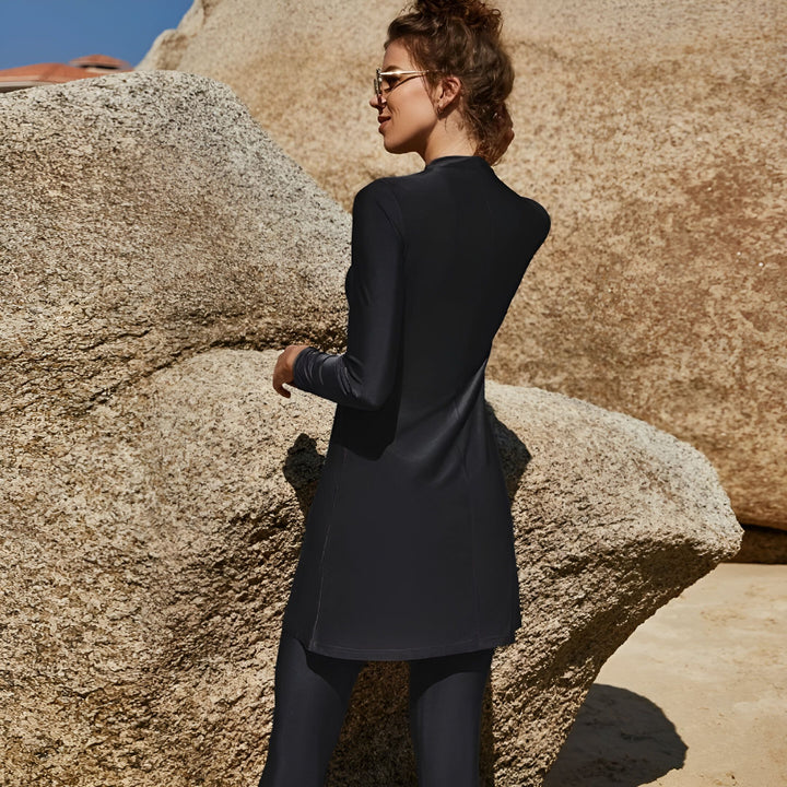 Femme portant un maillot de bain intégral noir sur une plage de sable. Burqini noir élégant pour femme, idéal pour la pudeur et la protection solaire. Vêtement de bain islamique moderne. Mode de plage modeste.