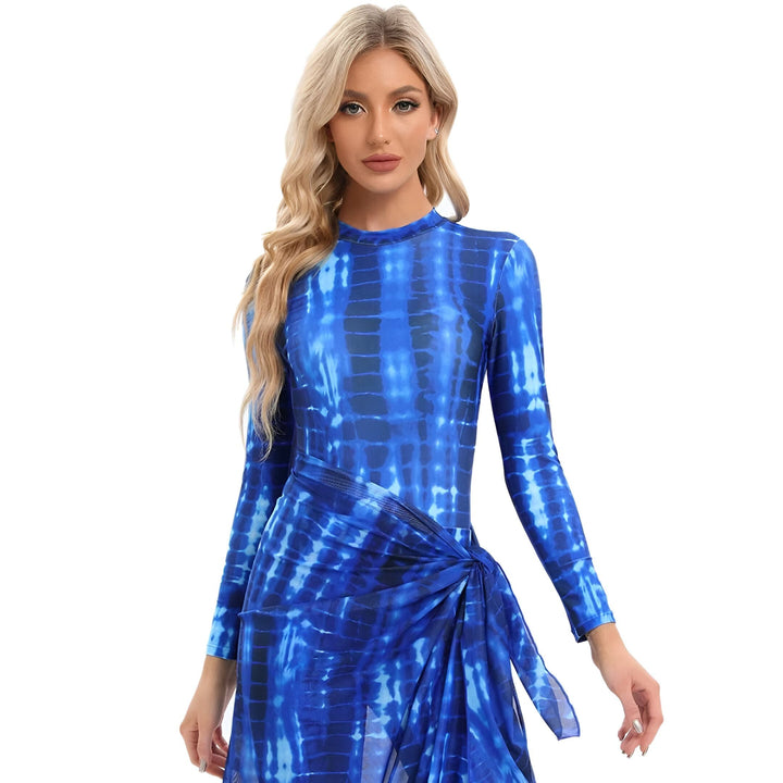 Femme blonde portant une robe longue bleue à motif tie-dye, avec une ceinture nouée sur le côté. Style estival et décontracté.