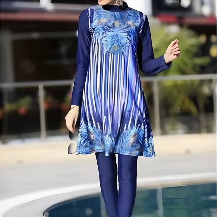 Femme portant un maillot de bain intégral bleu imprimé, hijab assorti, debout près de la piscine. Lunettes de soleil dans la main. Mode modeste et bain couvrants.