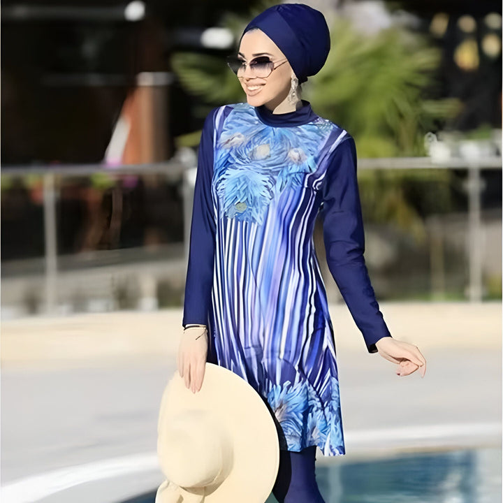 Femme élégante en burkini bleu avec motifs, foulard assorti et lunettes de soleil près d'une piscine. Elle tient un chapeau de paille. Mode de bain islamique moderne.