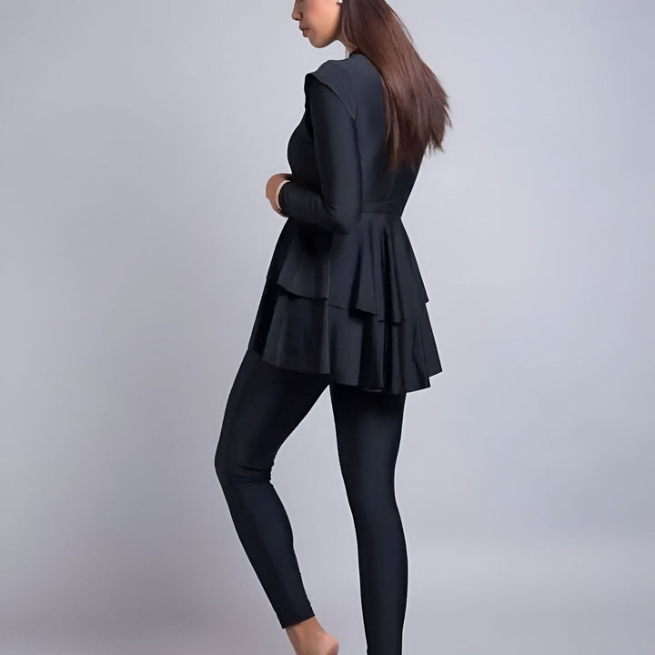 Femme en maillot de bain intégral noir avec haut à volants et legging, manches longues. Vêtement de bain pudique moderne.
