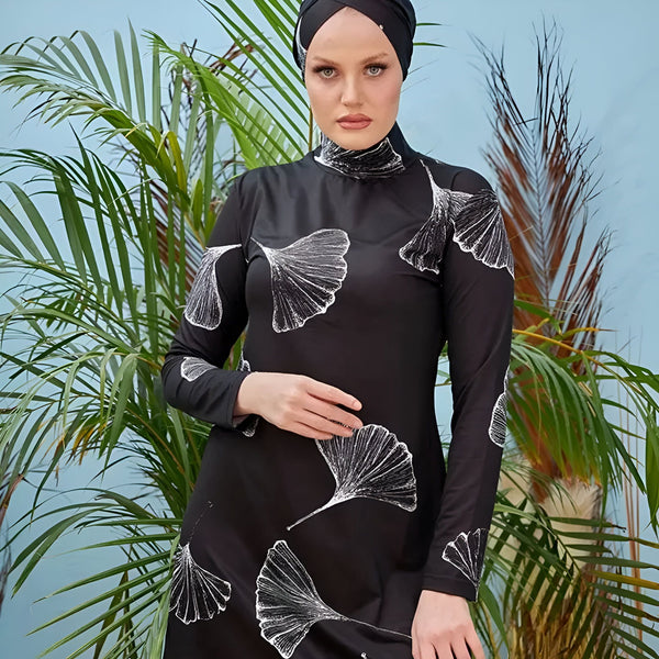 Femme portant un burkini noir à motifs de feuilles blanches, voile noir assorti. Vêtements de bain islamiques à manches longues, style modeste. Mode pudique, vêtements de plage pour femmes musulmanes.