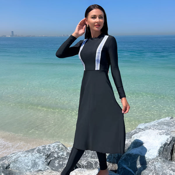 Tenue de bain modeste noire avec motifs blancs, legging noir assorti, chapeau de paille, petit gâteau et sac de plage. Ensemble élégant et respectueux pour la natation.