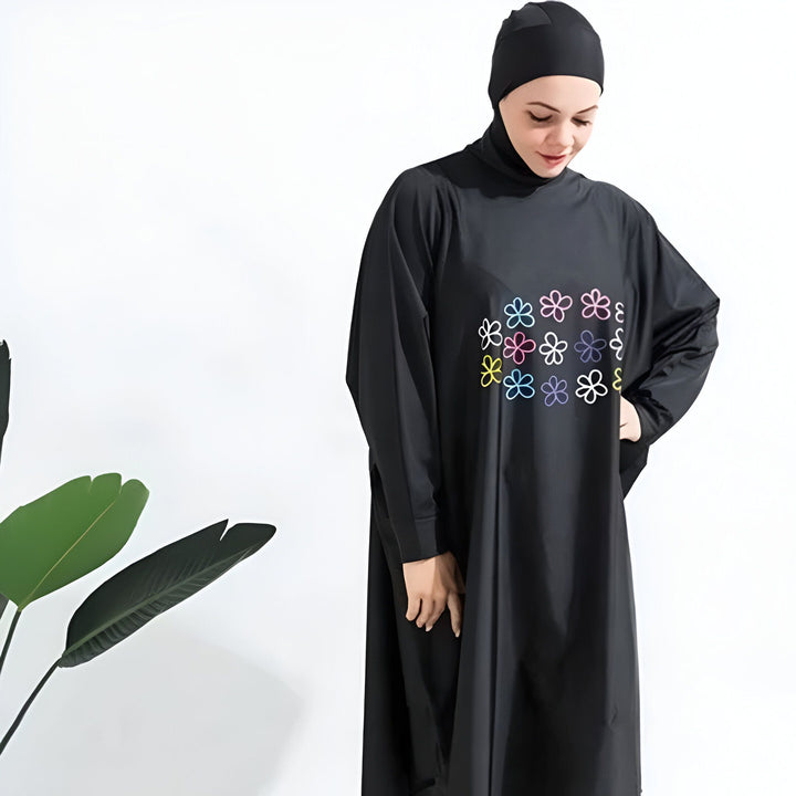 Femme portant un burkini noir à manches longues avec des motifs floraux colorés. Vêtement de bain modeste avec bonnet intégré.