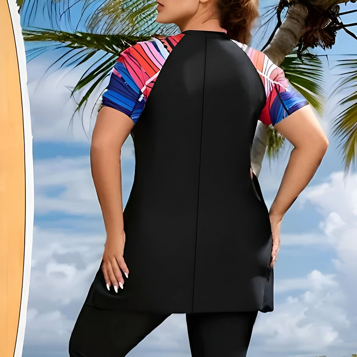 Femme en maillot de bain modeste noir et manches colorées, debout près d'une planche de surf et de palmiers sur une plage ensoleillée. Protection solaire et style pour les activités aquatiques.