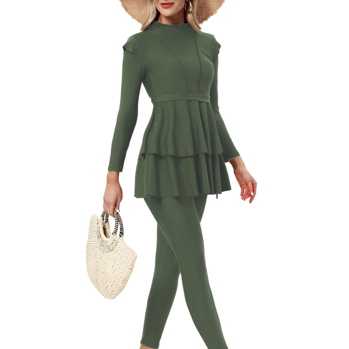 Une femme portant un maillot de bain burkini vert olive à manches longues avec un col montant et un motif à volants à deux niveaux, associé à un legging. Vêtement de bain modeste pour femme.