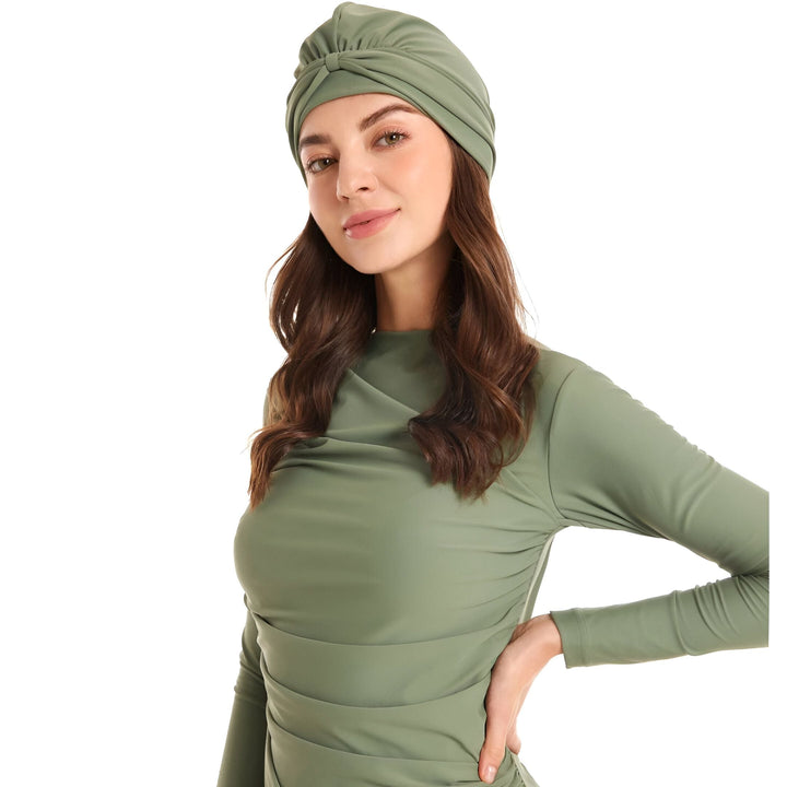 Portrait d'une jeune femme portant un maillot de bain intégral vert olive et un turban assorti. Elle regarde la caméra avec une expression douce. Le fond est blanc.