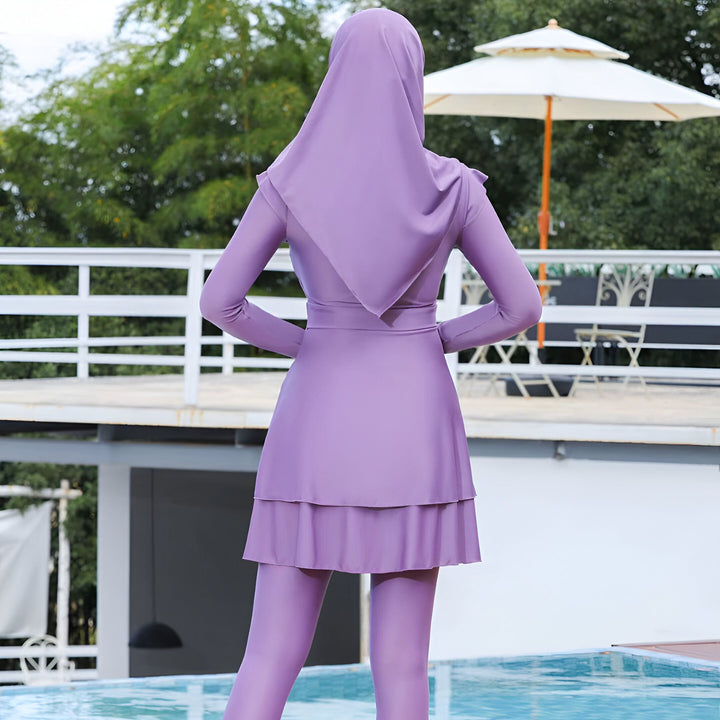 Vue arrière d'une femme portant un maillot de bain intégral violet avec hijab, debout près d'une piscine. Mode de bain modeste, burkini.