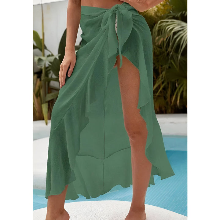 Vue arrière d'une femme en bikini blanc et paréo transparent, posant près d'une piscine turquoise avec des palmiers. Style vacances, été, mode balnéaire.