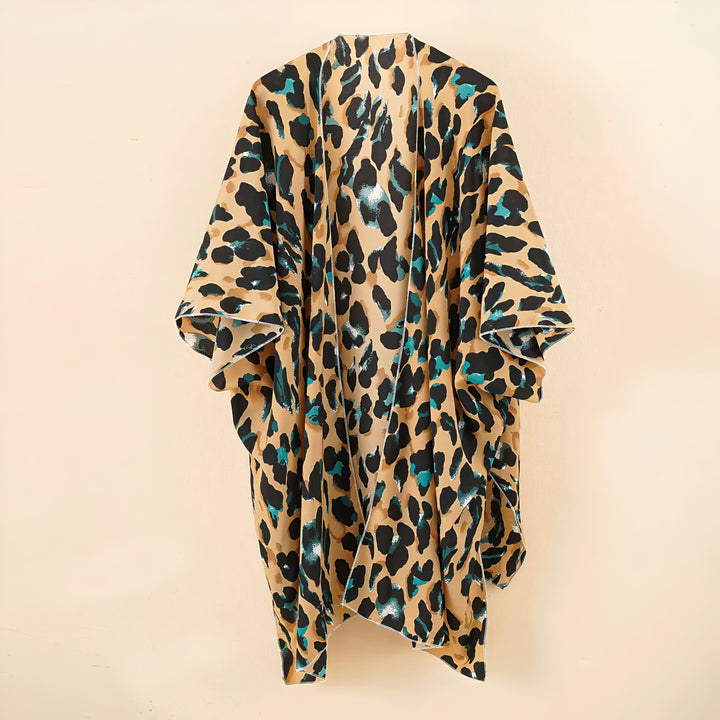 Kimono long à motif léopard beige, noir et turquoise suspendu devant un mur couleur crème. Vêtement d'extérieur ample et léger.