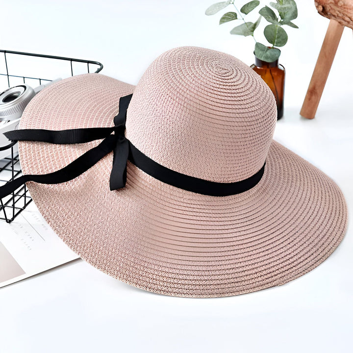 Vue rapprochée d'un chapeau de paille bleu marine à large bord avec un ruban noir, une caméra vintage, un magazine et un petit vase. Élégant accessoire de mode pour femme. Style estival.