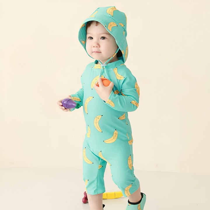 Bébé portant une combinaison et un chapeau assortis, imprimés de pêches souriantes, jouant avec un bloc jaune. Vêtements de bébé mignons et confortables pour jouer.