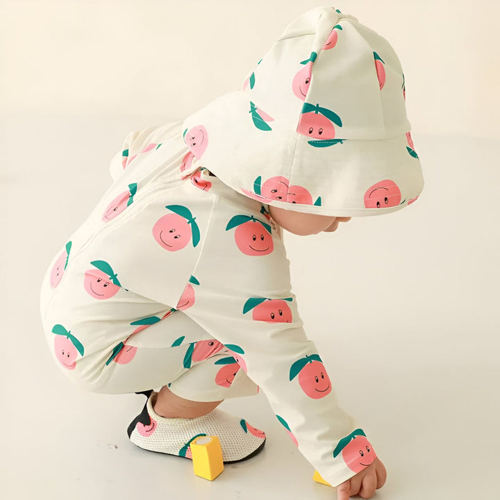 Un bébé porte un maillot de bain turquoise à motifs de bananes et un chapeau assorti. Il tient des jouets de fruits colorés dans ses mains. Mode enfantine pour la plage et la piscine. Protection solaire pour les jeunes enfants.