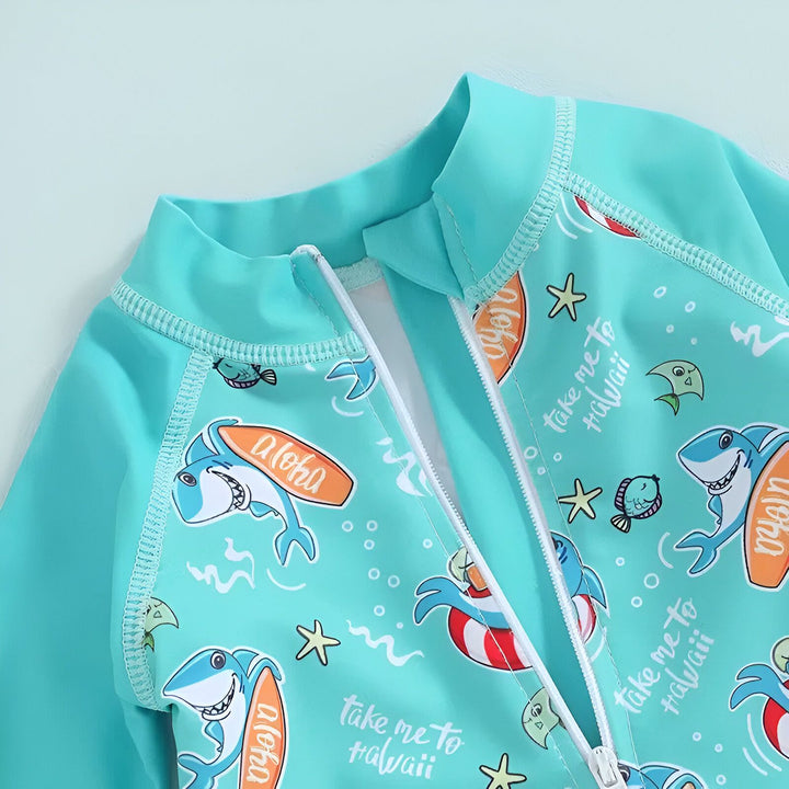 Combinaison de bain turquoise pour enfant, imprimée avec des motifs de requins, d'étoiles de mer et de poissons. Les requins portent des planches de surf "aloha" et des bouées. Inscriptions "Take me to Hawaii". Fermeture éclair blanche. Idéal pour la plage.