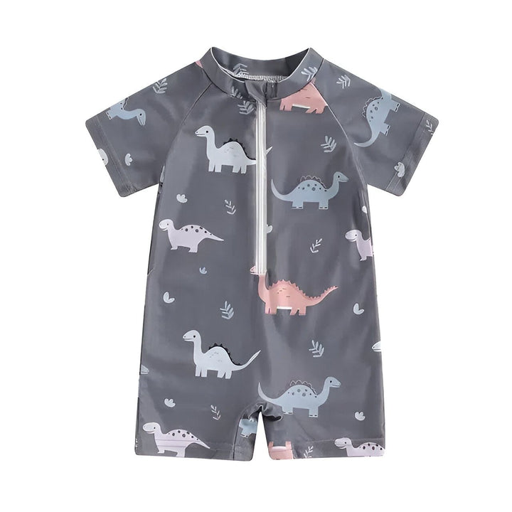 Combinaison de bain pour bébé grise à manches courtes avec des motifs de dinosaures roses et bleus. À côté, il y a une étoile de mer, un coquillage et des tranches de citron vert. Idéal pour la plage ou la piscine.