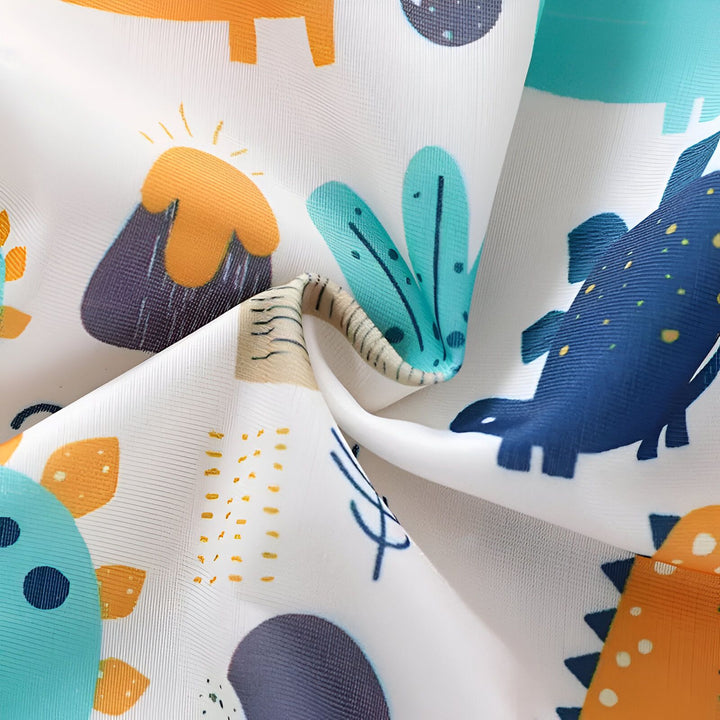 Gros plan d'un maillot de bain pour enfant avec un motif de dinosaures et de volcans sur du sable. Vêtements de plage pour enfants. Mode enfantine.